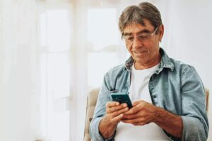 Homem sorridente usando smartphone em casa
