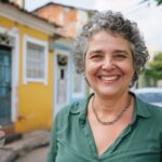 Mulher de mais ou menos 50 anos sorrindo e uma avenida.
