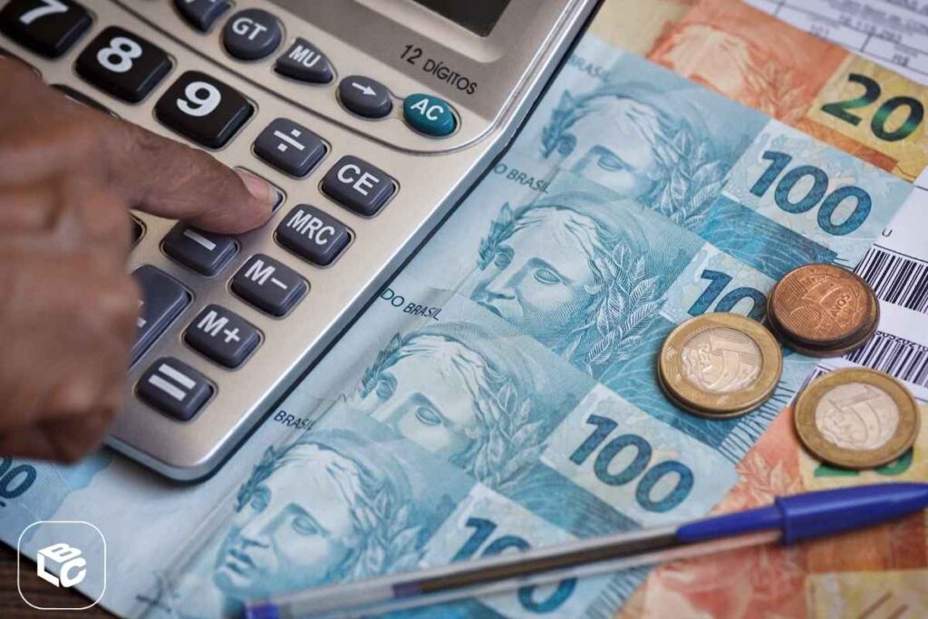 Pessoa usando calculadora ao lado de notas de real e moedas brasileiras, representando cálculo financeiro, controle de despesas e planejamento de dinheiro.